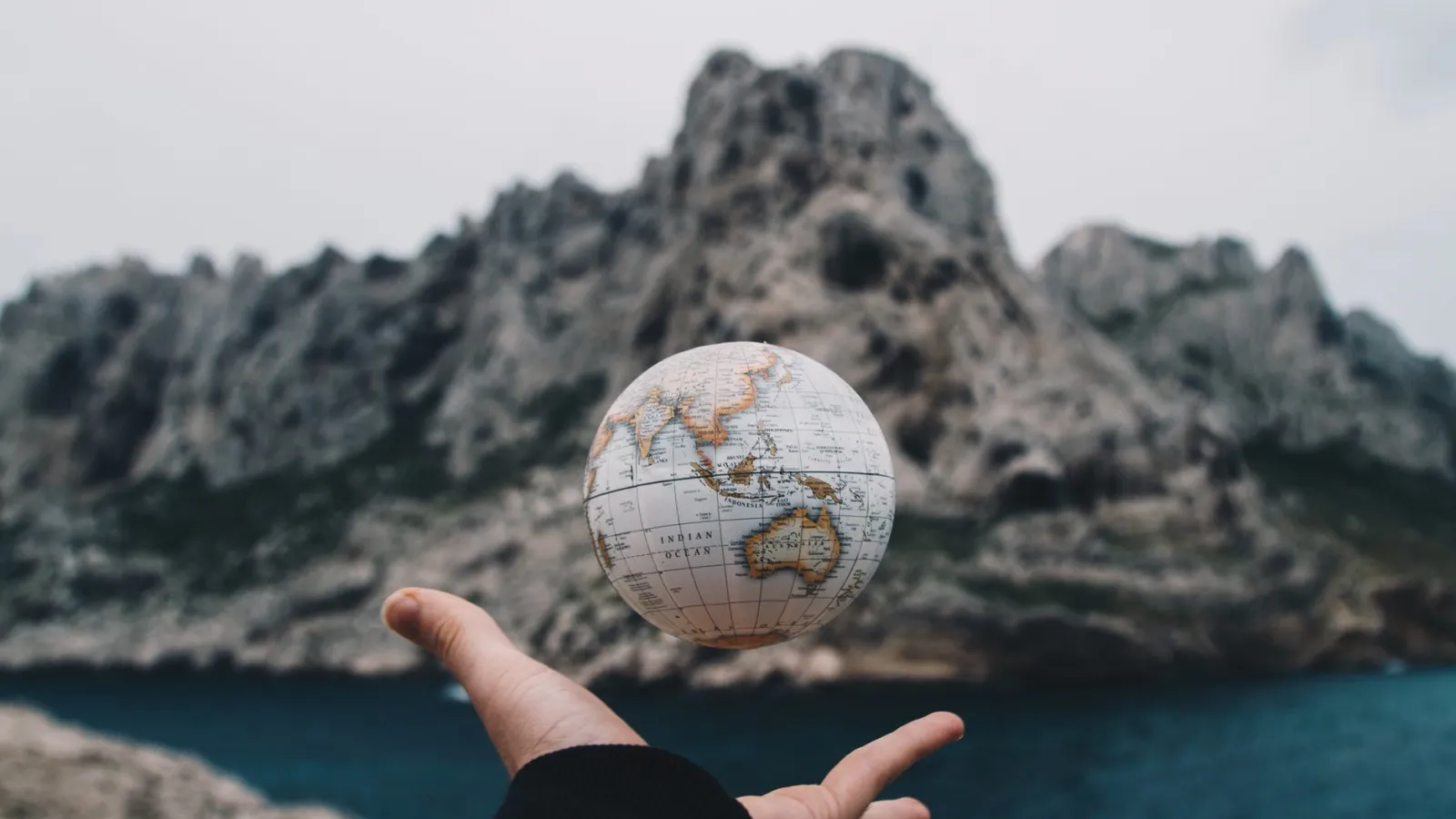 an image of a hand tossing a globe with a mountain in the background