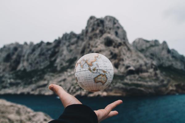 an image of a hand tossing a globe with a mountain in the background